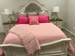 Un lit avec une couette rose, un plaid au point de crochet et plusieurs coussins.