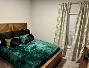 A bed with a wooden headboard, a green velvet bedspread, and multiple pillows.