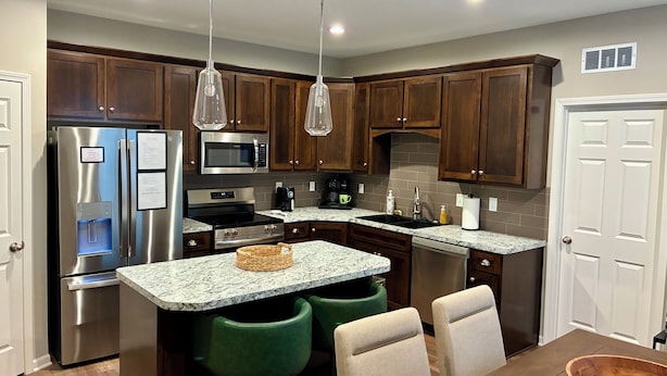 A modern kitchen with stainless steel appliances, wooden cabinets, granite countertops, and pendant lighting.