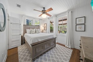 Ein Schlafzimmer mit einem Bett, einem Deckenventilator, einem Fenster mit Vorhängen und einer Holzkommode.