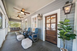 Eine Veranda mit Deckenventilatoren, einer Bank, Stühlen, einem Blumentopf und einer Tür mit Fenster.