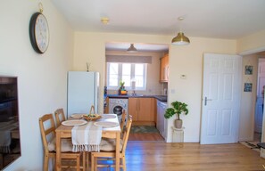 A compact kitchen with a washing machine, wooden dining table with chairs, and a white door. - Spacious Accommodation Near NEC & Birmingham Airport (Solihull)