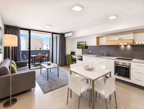 A modern apartment with a dining area, kitchen, and a sofa. - 2BR Walk to James St | Balcony + Parking (Brisbane)