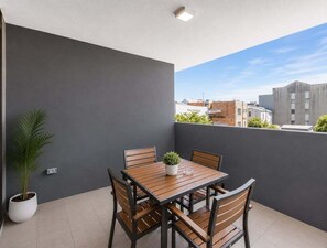 A balcony with a table and chairs, a potted plant, and a view of buildings. - 2BR Walk to James St | Balcony + Parking (Brisbane)