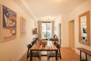 Ein Zimmer mit Esstisch, Stühlen, einer Couch, einem Fernseher und Bildern an den Wänden.