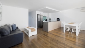 Eine moderne Küche mit einer zentralen Kochinsel, einem Essbereich mit weißen Stühlen und einem grauen Sofa mit Kissen.