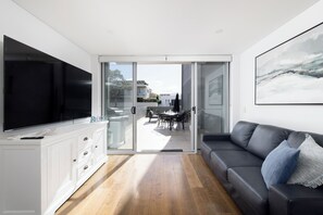 A modern living room with a flat-screen TV, a sofa, and a dining area visible through glass doors. - The Shoal at Shoal Bay (Shoal Bay)