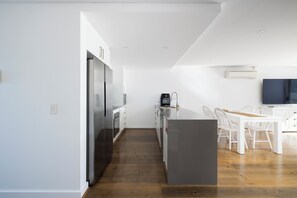 A modern kitchen with white cabinetry, a central island, and a dining area with white chairs. - The Shoal at Shoal Bay (Shoal Bay)
