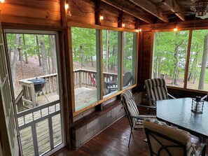 Une cabane en bois dotée de grandes fenêtres, d’une terrasse et d’une table avec des chaises.