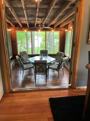 Un intérieur en bois avec une table ronde et des chaises, de grandes fenêtres et un ventilateur de plafond.