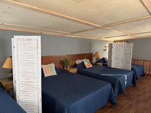 Een kamer met twee bedden, houten hoofdborden, een nachtkastje met lamp, een potplant en een garderobe.
