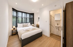 Ein modernes Schlafzimmer mit einem großen Bett, Nachttischen, einem Schreibtisch und einem Badezimmer mit Waschbecken und Spiegel.