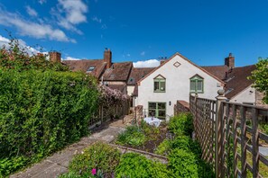Ein traditionelles Haus mit einem Gartenweg, der zum Eingang führt, umgeben von üppigem Grün und wolkenlosem, blauem Himmel.