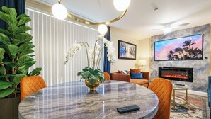 Uma sala de estar moderna com uma mesa redonda de mármore, cadeiras laranja, lareira, televisão e uma planta grande.