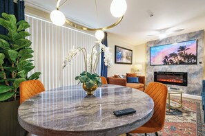 Ein modernes Wohnzimmer mit einem runden Marmortisch, orangefarbenen Sesseln, einem Kamin, einem Fernseher und einer großen Pflanze.