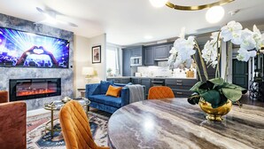 Uma sala de estar moderna com televisão, sofá, mesa de jantar e cozinha ao fundo.
