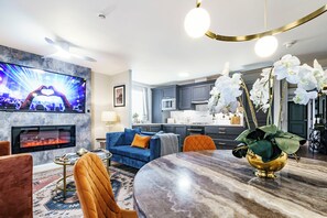 Ein modernes Wohnzimmer mit Fernseher, Sofa, Esstisch und einer Küche im Hintergrund.