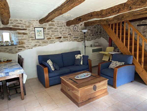 A rustic living room with a stone wall, wooden beams, a blue sofa, a wooden chest, and a staircase. - High-quality traditional Breton vacation rental in Gomene, with a pool, Wi-Fi, and gardens (GOMENE)