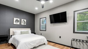 Ein modernes Schlafzimmer mit einem Bett, einem an der Wand montierten Fernseher und einem Fenster mit Jalousien.