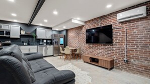 Ein moderner Wohnraum mit Küche, Essbereich und einem großen Flachbildfernseher an einer Ziegelwand.