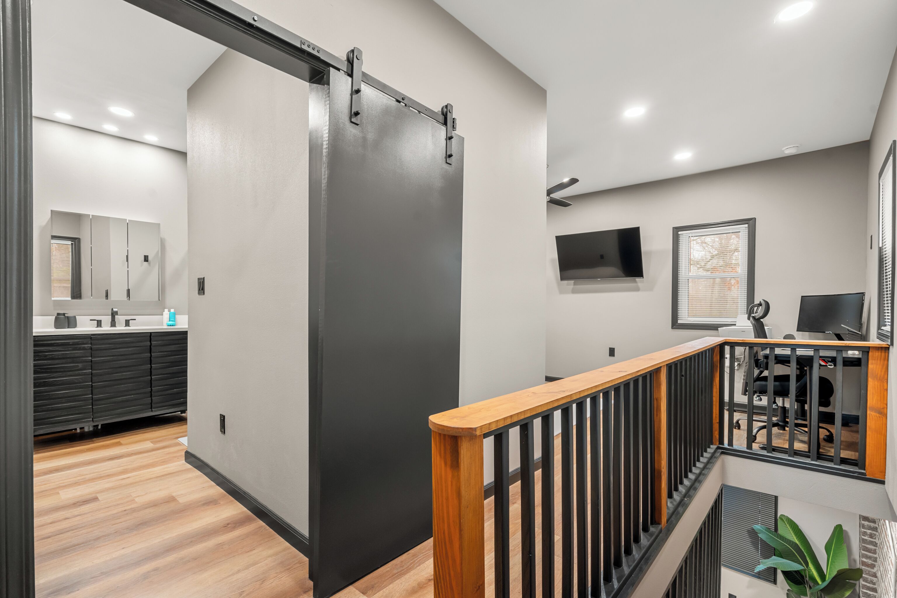 A modern interior with a sliding door, a staircase with wooden railings, a flat-screen TV, and a desk with a chair.