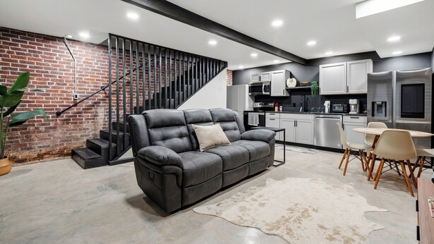 Ein modernes Wohnzimmer mit einer Ledersofa, einem Essbereich mit Stühlen, einer Küche mit Geräten und einer Treppe an einer Ziegelwand.