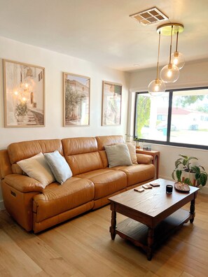 Ein Wohnzimmer mit einer Ledersofa, einem Holztisch und gerahmten Kunstwerken an der Wand.