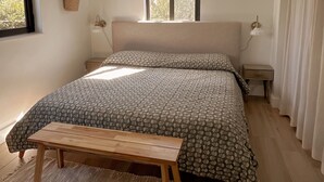 Quarto com cama, mesas de cabeceira, janela, planta pendurada e luminária no teto.