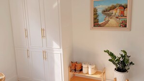 Quarto com um guarda-roupa branco, um sapateiro de madeira, um quadro emoldurado e um vaso de planta.