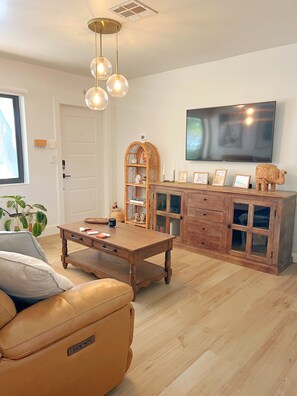 Ein Wohnzimmer mit Couch aus Leder, einem Holztisch, einem an der Wand befestigten Fernseher und einem Korbuscheinrichtungsstück.