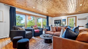 Ein modernes Wohnzimmer mit Holzbalkendecke, großen Fenstern und einer gemütlichen Sitzecke.