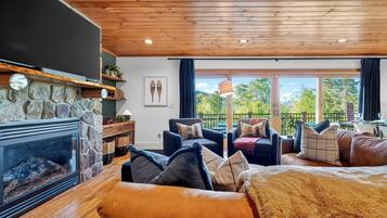 A cozy living room with a stone fireplace, wooden ceiling, and a balcony with outdoor furniture.