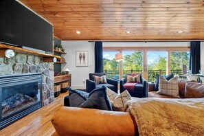 Een gezellige woonkamer met een stenen openhaard, houten plafond en een balkon met tuinmeubilair.