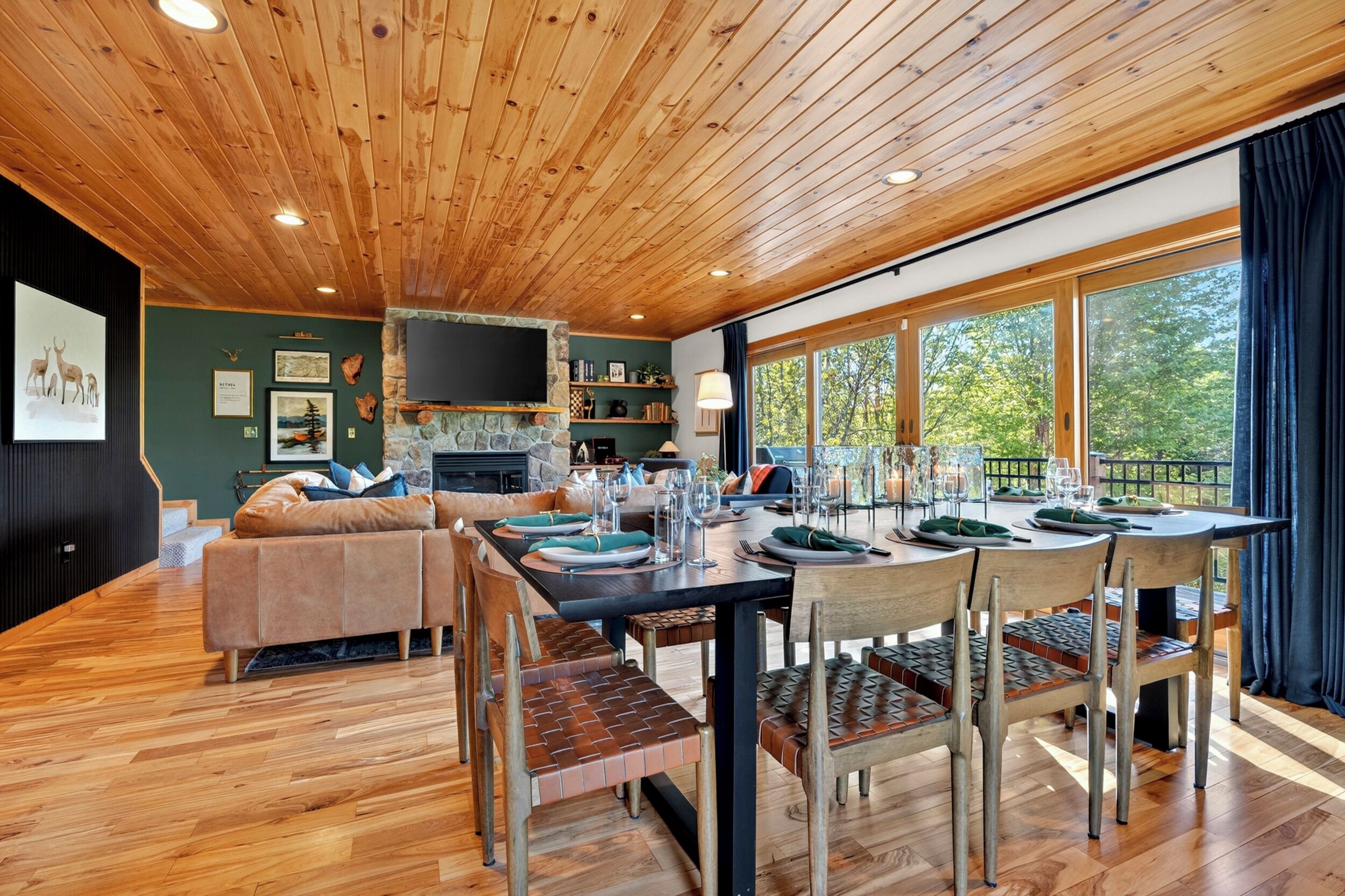 A wooden ceiling, a stone fireplace, a dining table with chairs, a sofa, and a TV mounted on the wall.