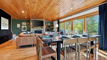 A wooden ceiling, a stone fireplace, a dining table with chairs, a sofa, and a TV mounted on the wall.