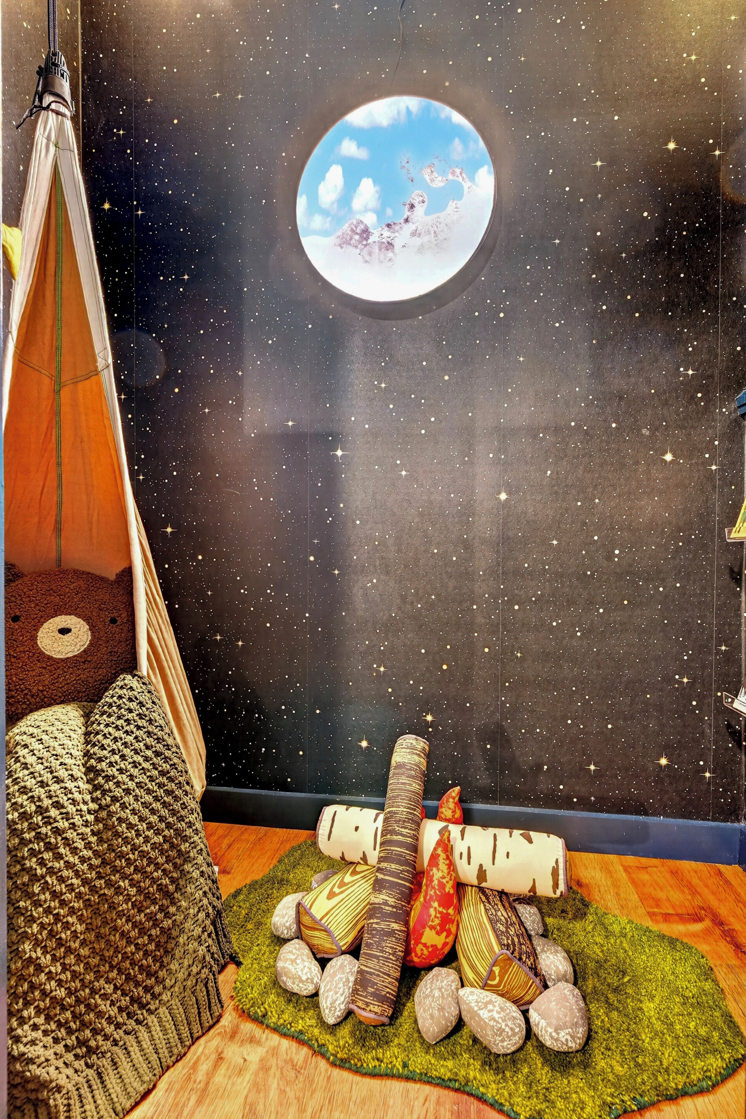 Ein Zimmer mit Sternenhimmel, einem Rundfenster, einem Zelt und einer kleinen Feuerstelle.