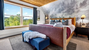 Ein Schlafzimmer mit großem Fenster, einem Bett mit vielen Kissen, einer Bank und einem Wandgemälde.
