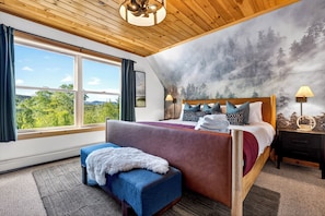 A bedroom with a large window, a bed with multiple pillows, a bench, and a wall mural. - Ultimate Family Adventure Basecamp: Golf Sim, Rock Wall, Hot Tub, Sauna & More (Bethel)
