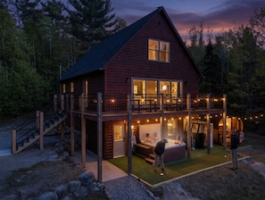 A log cabin with a balcony, hot tub, and a deck area. - Ultimate Family Adventure Basecamp: Golf Sim, Rock Wall, Hot Tub, Sauna & More (Bethel)