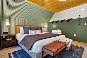 A neatly arranged bedroom with a bed, bedside lamps, a nightstand, a bench, and a wall-mounted light fixture.