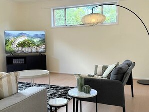 Ein Wohnzimmer mit Fernseher, der ein Landschaftsbild zeigt, einer Couch, einem kleinen runden Tisch und einer Hängelampe.