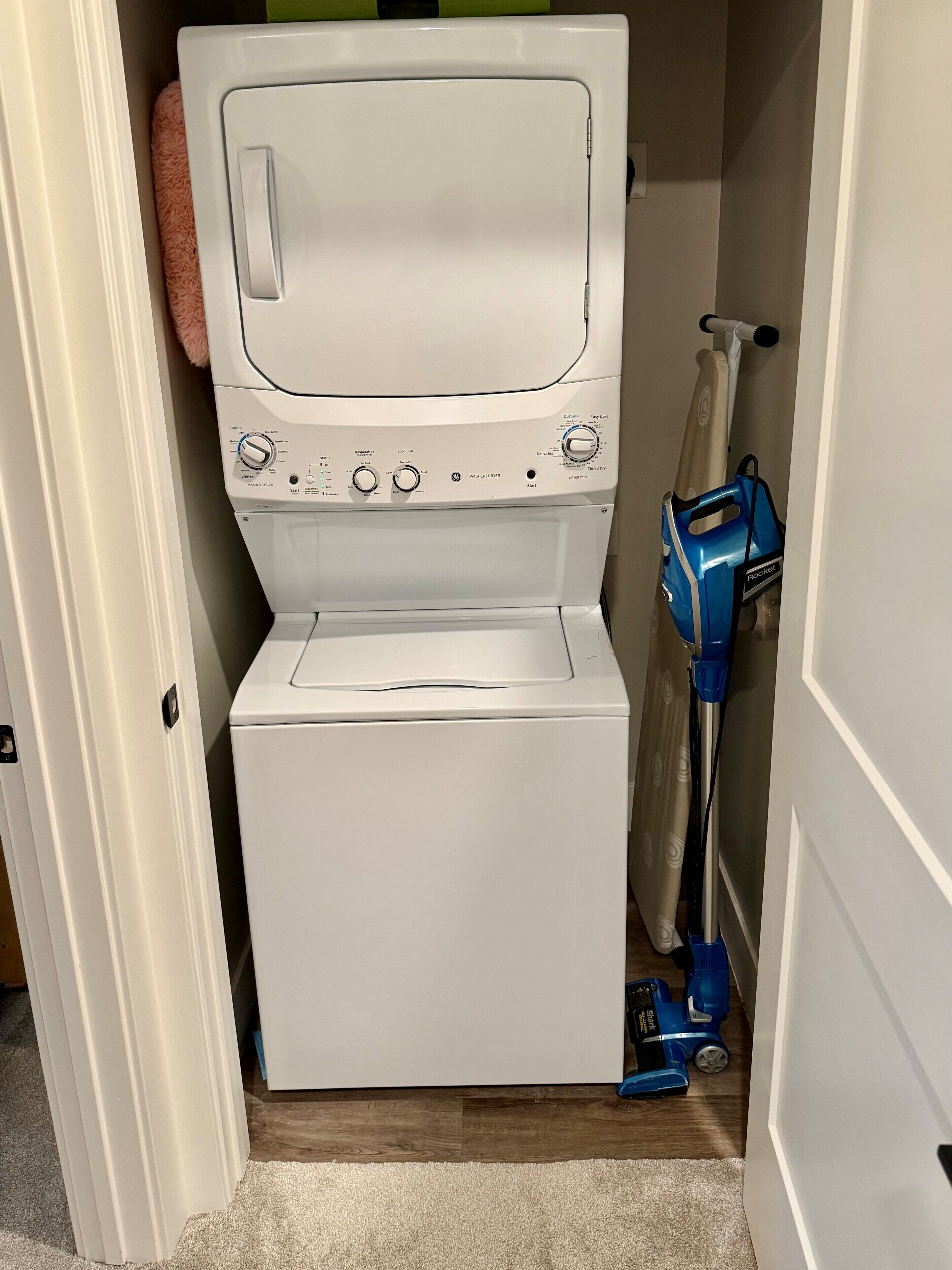A compact laundry room with a white washer and dryer, a blue vacuum cleaner, and a mop.