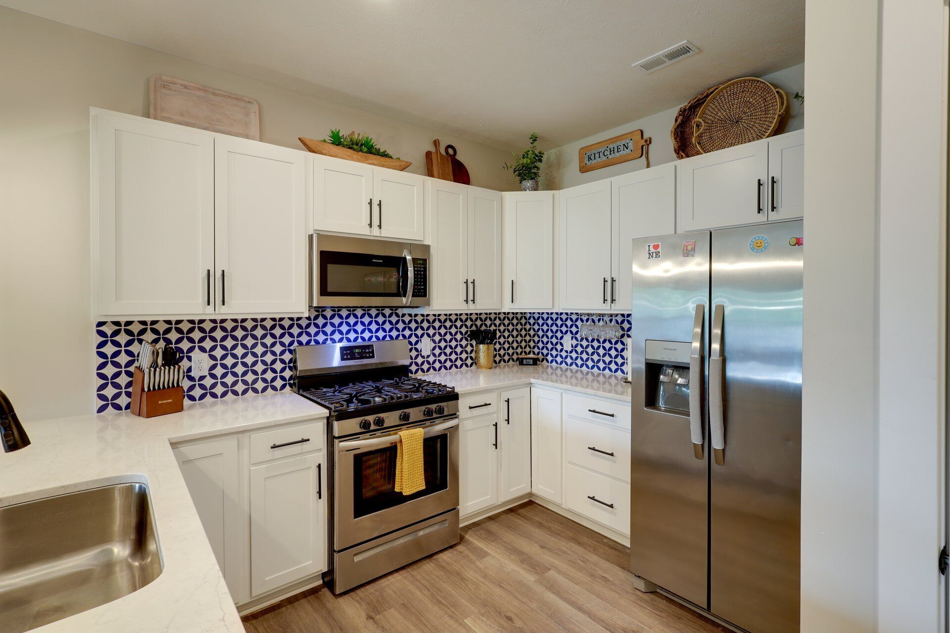 A modern kitchen with white cabinets, stainless steel appliances, and a patterned backsplash.