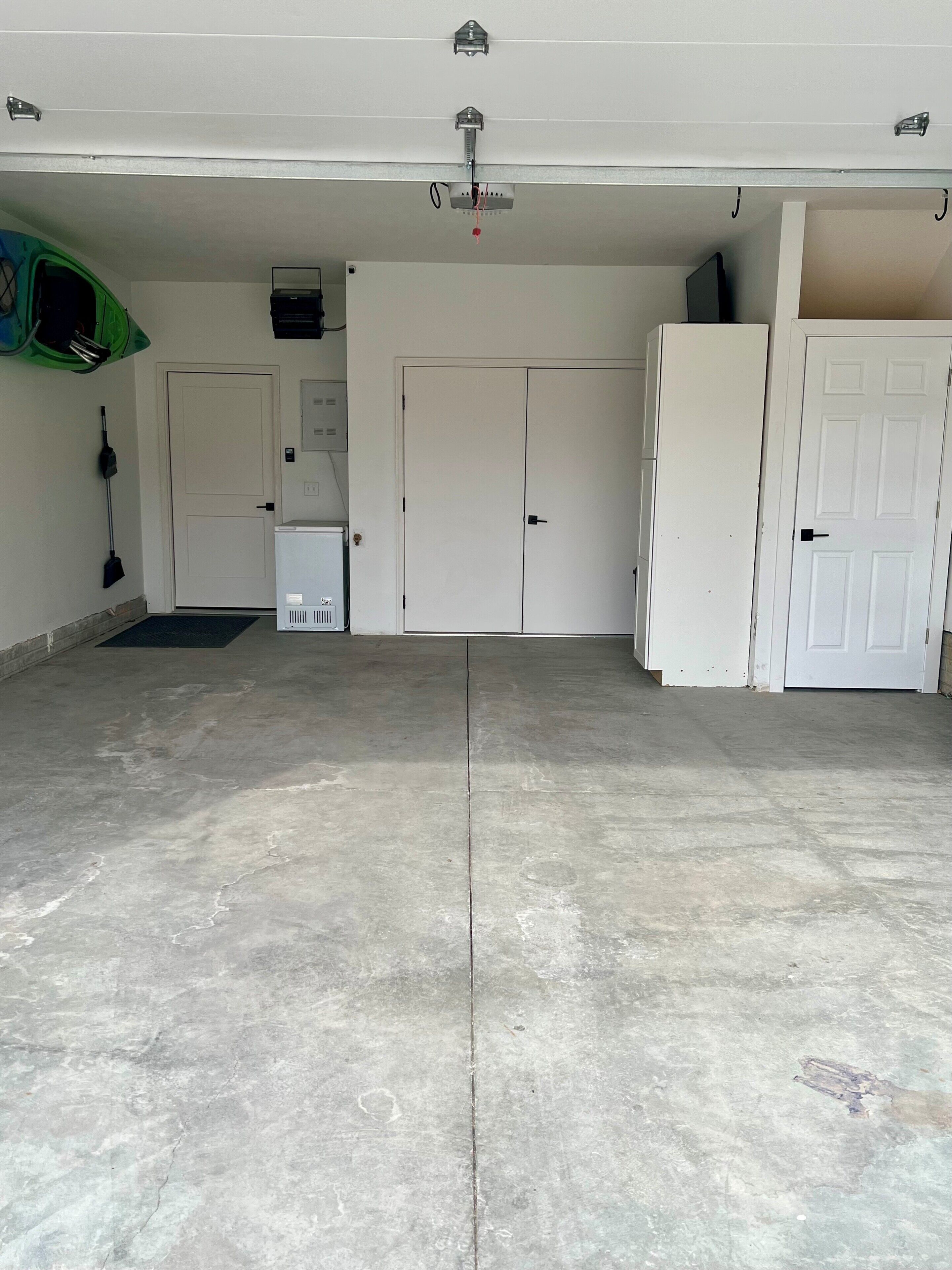 A spacious garage with concrete flooring, a white door, a white cabinet, and a green object on the left.