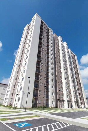A high-rise residential building with multiple balconies, a parking area with a disabled parking space, and a clear blue sky.
