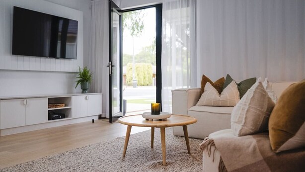 Uma sala de estar moderna com uma TV de tela plana, um sofá, uma mesa de centro e vista através de uma porta de vidro.