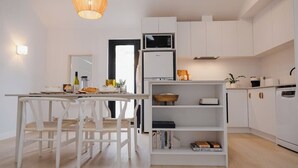 Uma cozinha moderna com armários brancos, uma área de refeições com cadeiras brancas e um lustre.