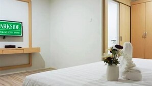 A hotel room with a bed, a wooden floor, a wall-mounted TV, and a wooden wardrobe. - Sovrano Hotel Batam (Batam)
