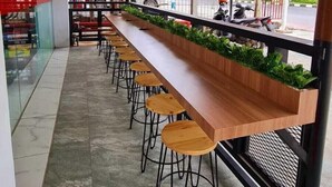 A long wooden bench with stools, a tiled floor, and a view of the street outside. - Sovrano Hotel Batam (Batam)