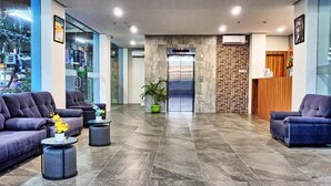 A modern lobby with two sofas, a reception desk, an elevator, and a potted plant. - Sovrano Hotel Batam (Batam)